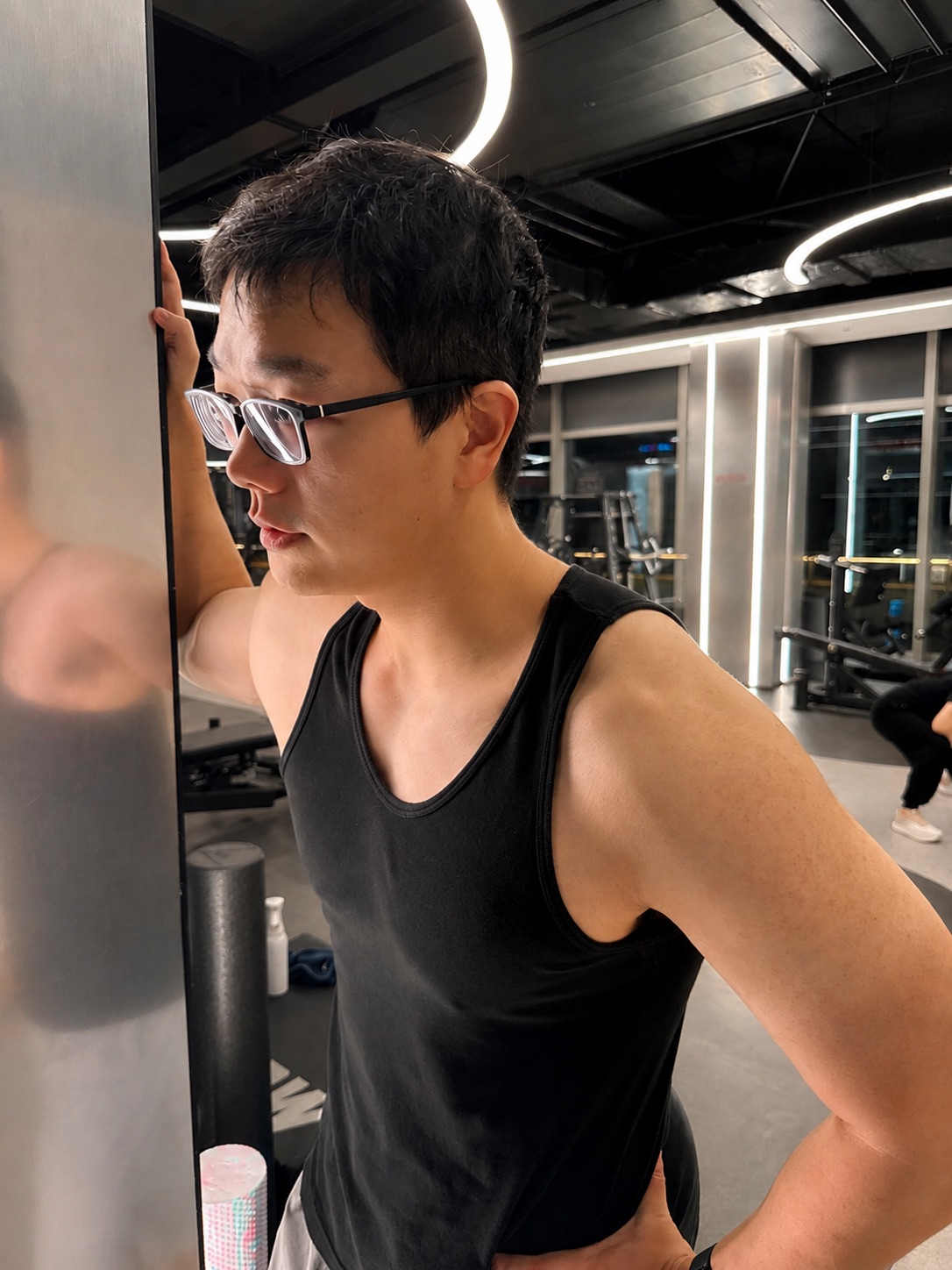 Azhe leaning on the gym mirror, shoulder and arm definition visible