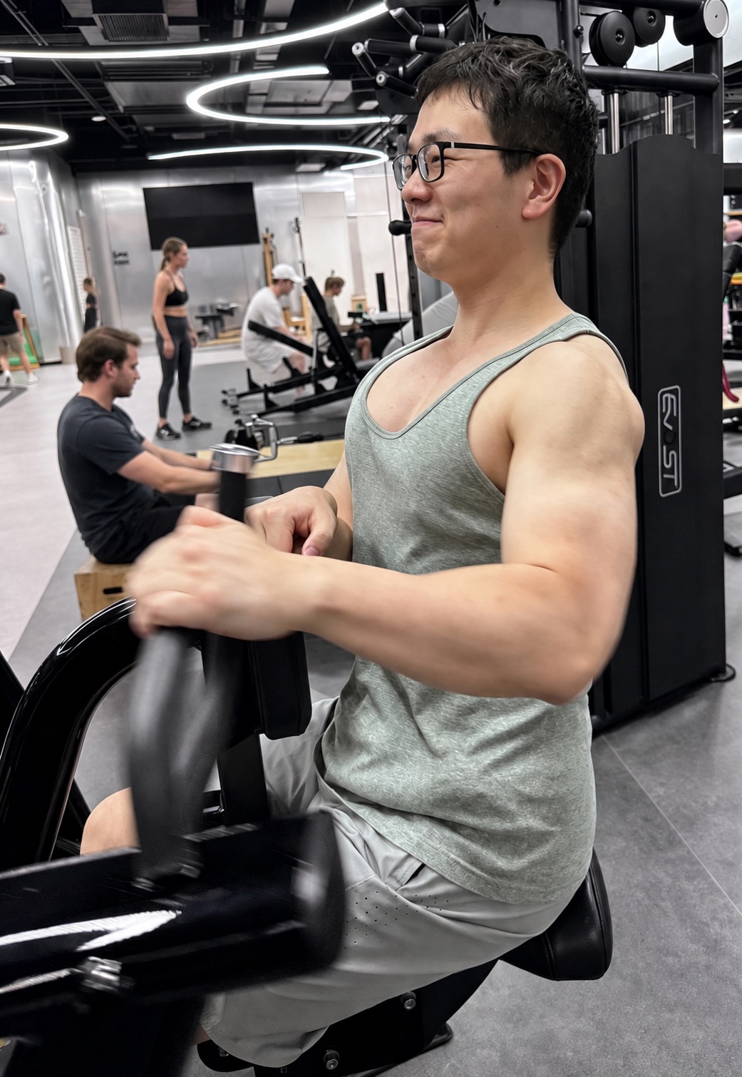 Azhe mid-session on a seated machine at the gym, in a tank top